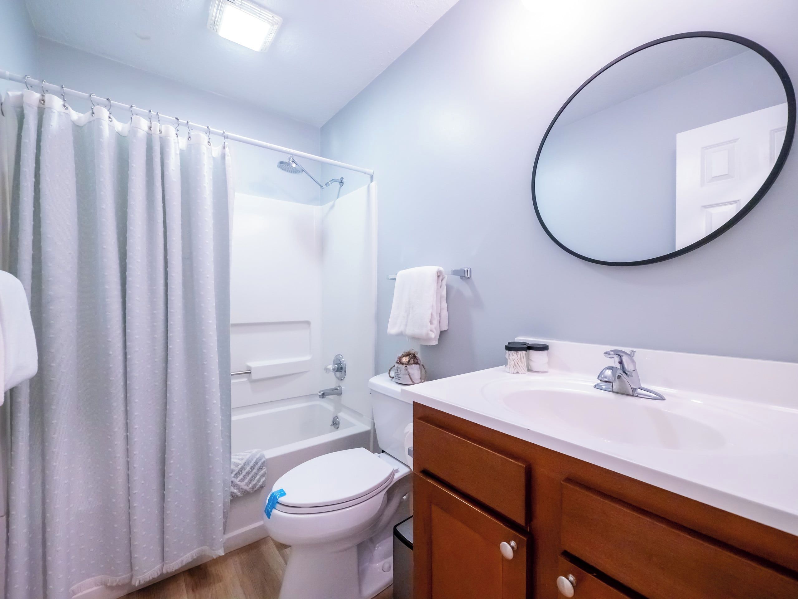 A bathroom with a bathtub, toilet, vanity, and a round mirror.