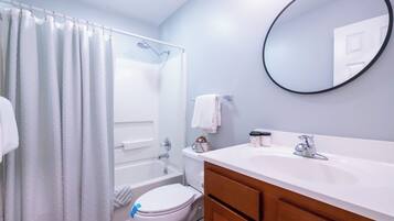 A bathroom with a bathtub, toilet, vanity, and a round mirror.