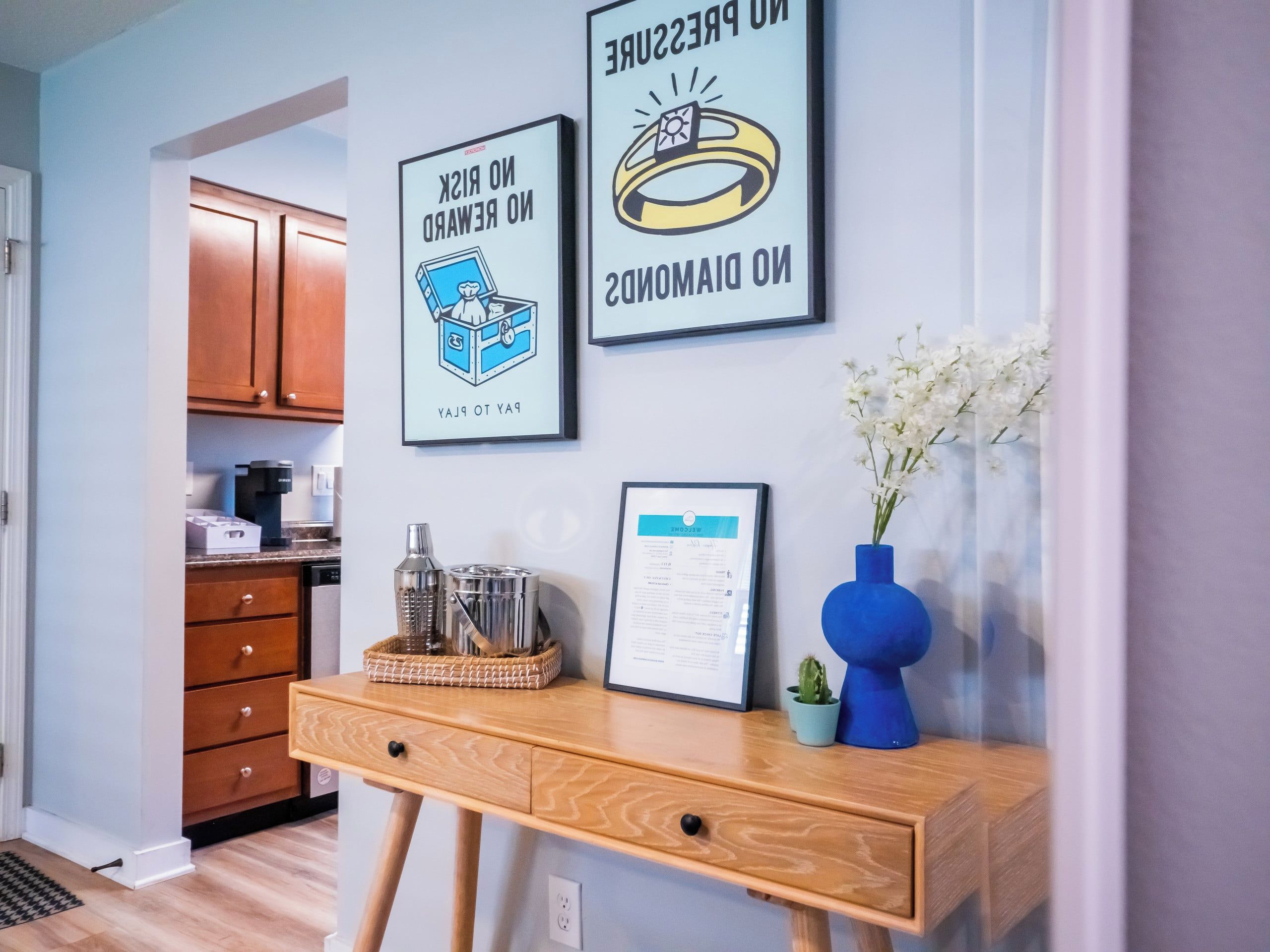 A kitchen area with wooden cabinets, a coffee maker, a framed certificate, and a desk with a vase of flowers.