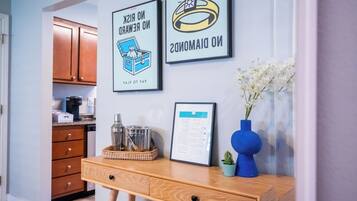 A kitchen area with wooden cabinets, a coffee maker, a framed certificate, and a desk with a vase of flowers.