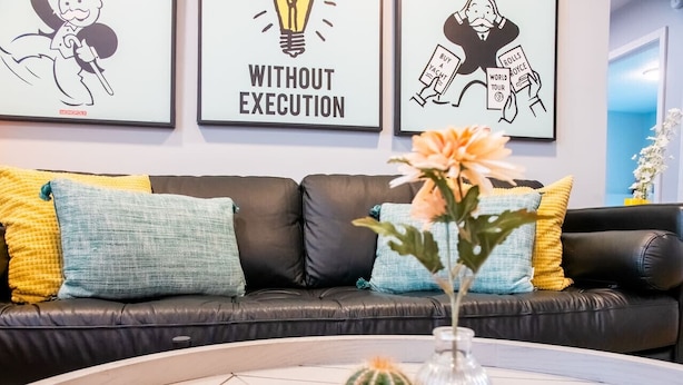 A modern living room with a leather sofa, colorful cushions, a round coffee table with a cactus and a vase, and framed artwork on the wall. - Playful, walkable, and comfortable, just steps from Mass Street. (Lawrence)