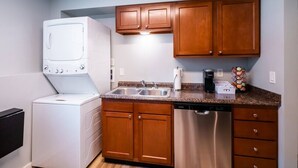 A compact kitchen with wooden cabinets, a built-in dishwasher, a double sink, and a stacked washer and dryer. - Playful, walkable, and comfortable, just steps from Mass Street. (Lawrence)
