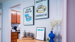 A kitchen with wooden cabinets, a coffee maker, and a framed menu on the wall. - Playful, walkable, and comfortable, just steps from Mass Street. (Lawrence)