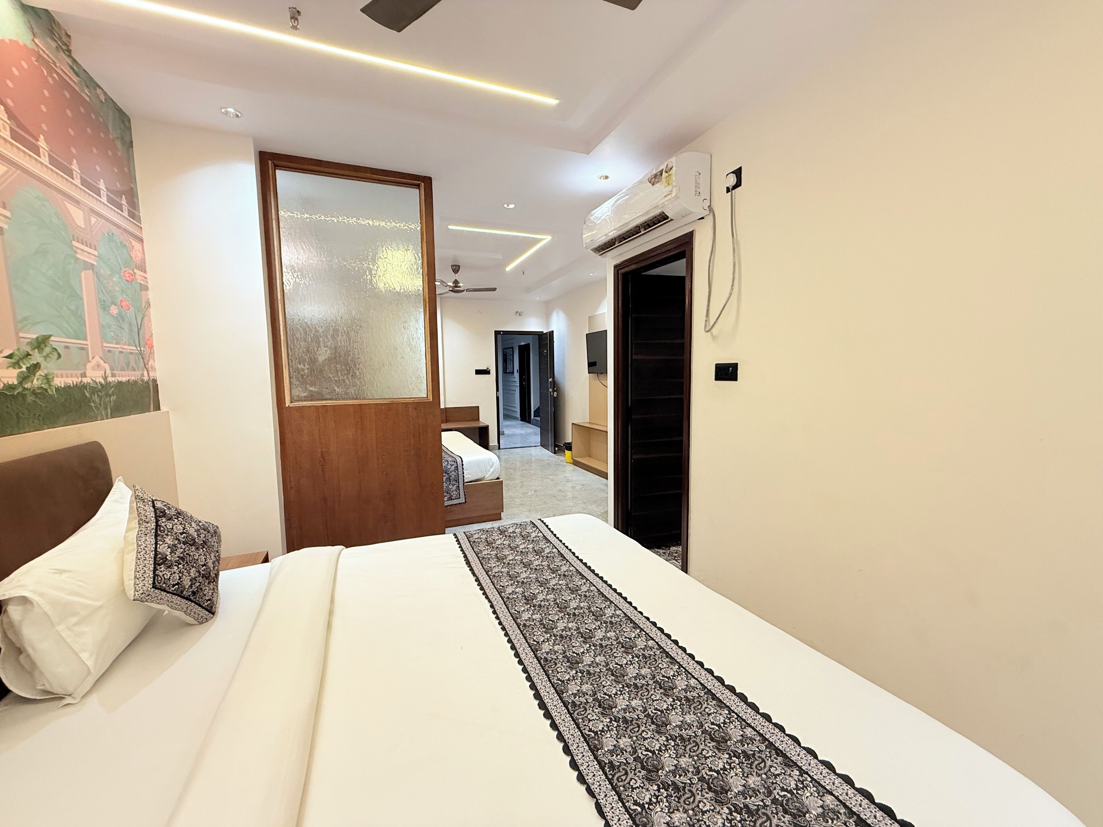 A hotel room with a bed, a large mirror, an air conditioning unit, and a hallway leading to another room.