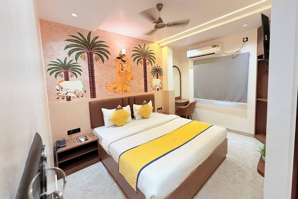 A modern hotel room with a large bed, a desk, a chair, and a ceiling fan.