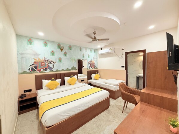 A hotel room with a large bed, a smaller bed, a desk, a chair, a ceiling fan, and a wall with decorative artwork.