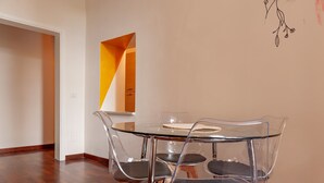 A dining area with a glass table and four chairs, a wooden floor, and a white wall with a geometric decoration. - 'Borghetto House - Pisa' Apartment with Private Terrace and Wi-Fi (Pisa)
