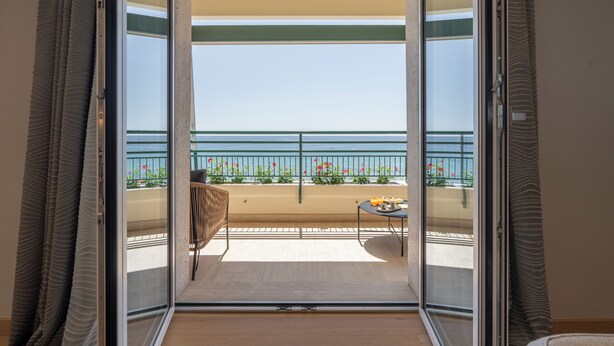 A balcony with a view of the sea, a table with a chair, and a small table with items on it.