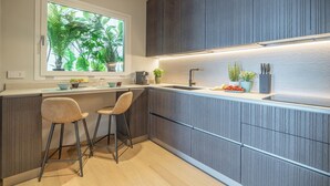 A modern kitchen with a window, two bar stools, and a countertop with plants and kitchenware.