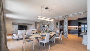 A modern dining area with a long table, white chairs, and a chandelier.