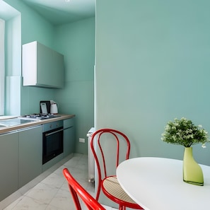 Une cuisine compacte équipée d’une cuisinière, d’un four et de placards, une table à manger agrémentée d’un vase, et une chaise rouge.