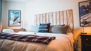 A neatly made bed with a plaid blanket, a pillow with a quote, and a framed picture of a skier on the wall.