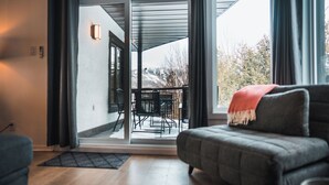 A modern living room with a grey sofa, a black rug, and a view of a patio with outdoor furniture and a snowy landscape.