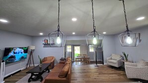 A spacious living room with a wooden floor, a large brown sofa, two armchairs, a TV, and pendant lights. - A+ location: UT, Melton Hill Parks, ORNL, shops (Oak Ridge)