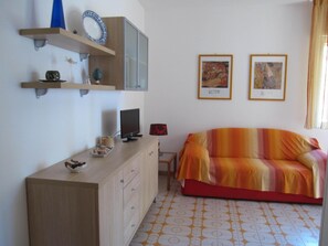 A room with a wooden dresser, a television, a colorful sofa, and two framed artworks on the wall. - Grado Pineta Flat With Terrace (Grado)