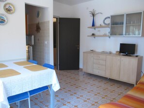 Quarto com uma mesa de jantar, cadeiras, televisão em um móvel e piso estampado.
