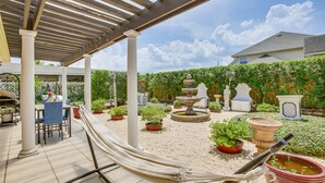 A covered patio area with a hammock, outdoor furniture, potted plants, and a decorative fountain. - Charming 3-bedroom house in delightful New Orleans with AC (New Orleans)