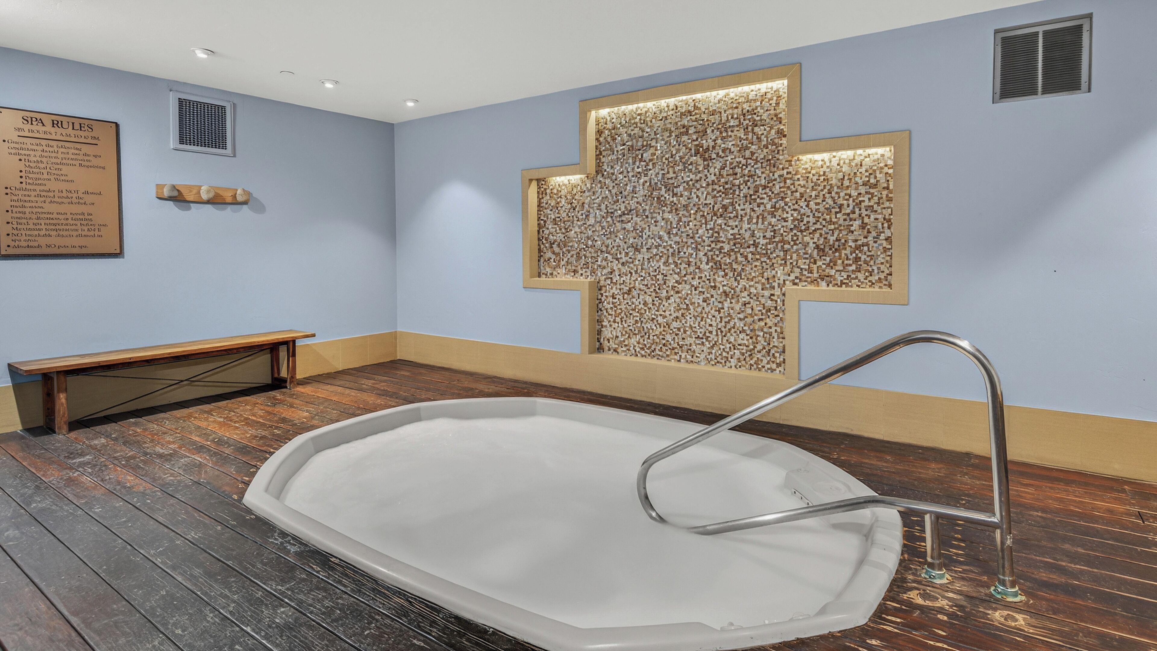 A spa room with a wooden bench, a wall-mounted cross, and a hot tub.