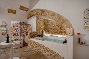 A spa area with a mosaic wall, a bathtub, and a table with a bottle and glasses. - GuestHost - Charming room of about 40 square meters, ideal for two people, located on the ground floor of a historic building (there is a small step at the entrance). Furnished with taste and attention to detail, it offers a warm and suggestive atmospher (Bari)