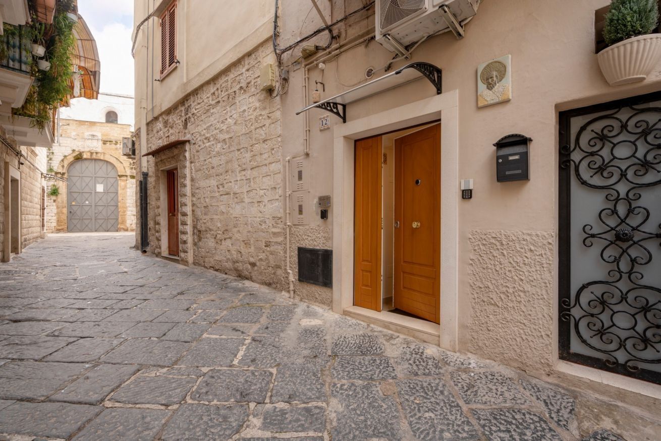 A narrow stone-paved street with a building featuring a wooden door and a metal gate.