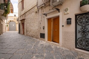 A narrow stone-paved street with a building featuring a wooden door and a metal gate. - GuestHost - Charming room of about 40 square meters, ideal for two people, located on the ground floor of a historic building (there is a small step at the entrance). Furnished with taste and attention to detail, it offers a warm and suggestive atmospher (Bari)