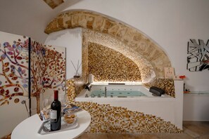 A spa area with a mosaic wall, a bathtub, and a wine bottle on a table. - GuestHost - Charming room of about 40 square meters, ideal for two people, located on the ground floor of a historic building (there is a small step at the entrance). Furnished with taste and attention to detail, it offers a warm and suggestive atmospher (Bari)