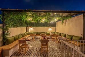 An outdoor seating area with tables and chairs, a patterned floor, and a pergola with hanging lights. - Riad JABADOR De Marrakech (Marrakech)