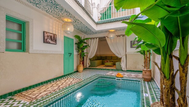 An indoor swimming pool with a tiled floor, a green door, and a seating area with a table and chairs. - Riad JABADOR De Marrakech (Marrakech)