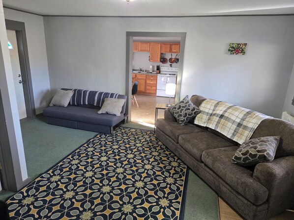 A living room with a sofa, a patterned rug, and a couch with a plaid throw. - WP2 – 1BR Apt for 6 Near Trails & Dining Between Houghton & Calumet w/EV Outlet (Calumet)