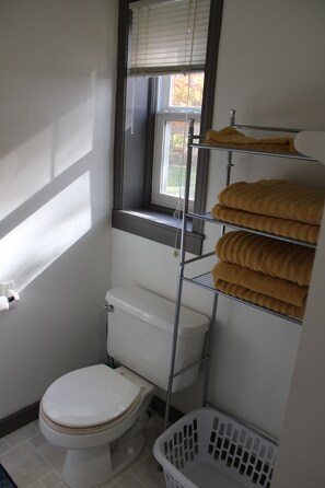 A small bathroom with a toilet, a window, and a metal shelf holding towels. - WP2 – 1BR Apt for 6 Near Trails & Dining Between Houghton & Calumet w/EV Outlet (Calumet)
