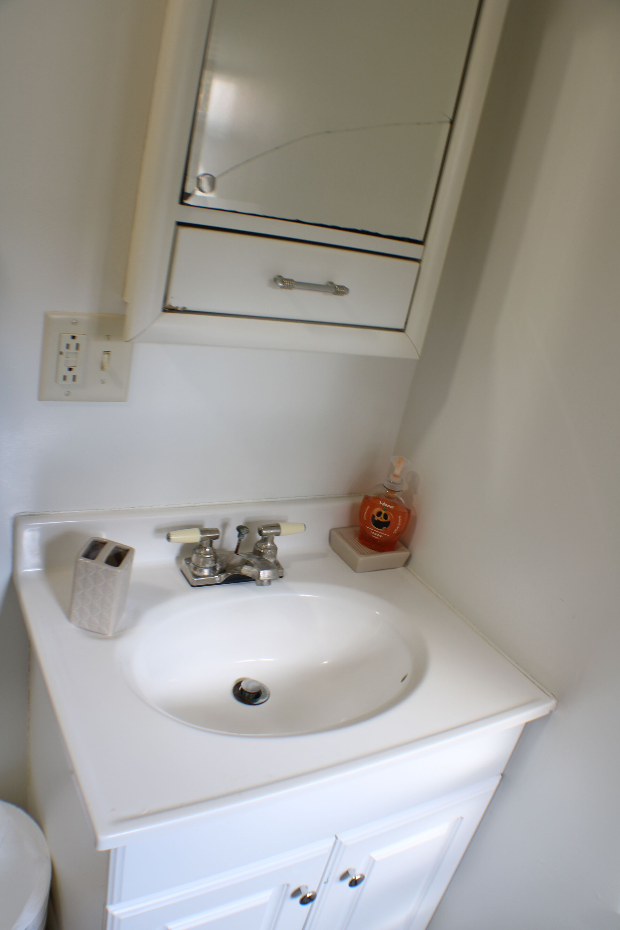 Une salle de bain avec un lavabo blanc, un miroir au-dessus et un petit flacon orange posé sur le comptoir.