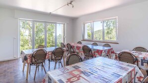 A dining area with multiple tables and chairs, large windows with a view of greenery, and a ceiling with a visible light fixture. - CLOS ST FRANCOIS SPA (Wangenbourg-Engenthal)