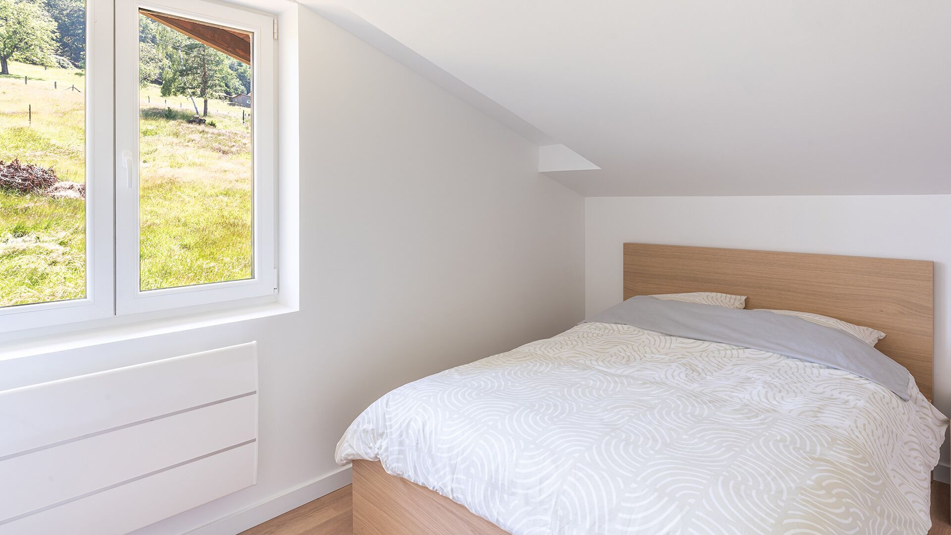A bedroom with a bed, a window, and a view of a grassy area.