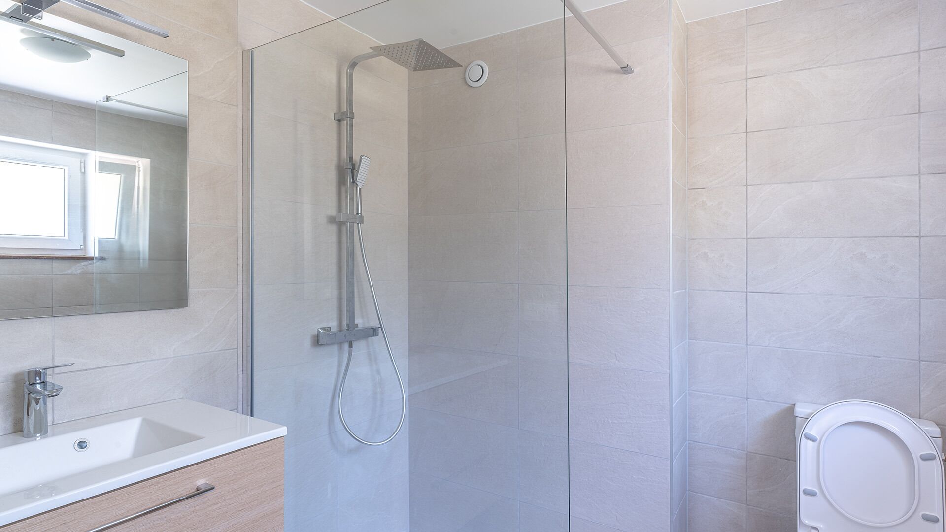 Un baño moderno con ducha de vidrio, lavamanos blanco y retrete.