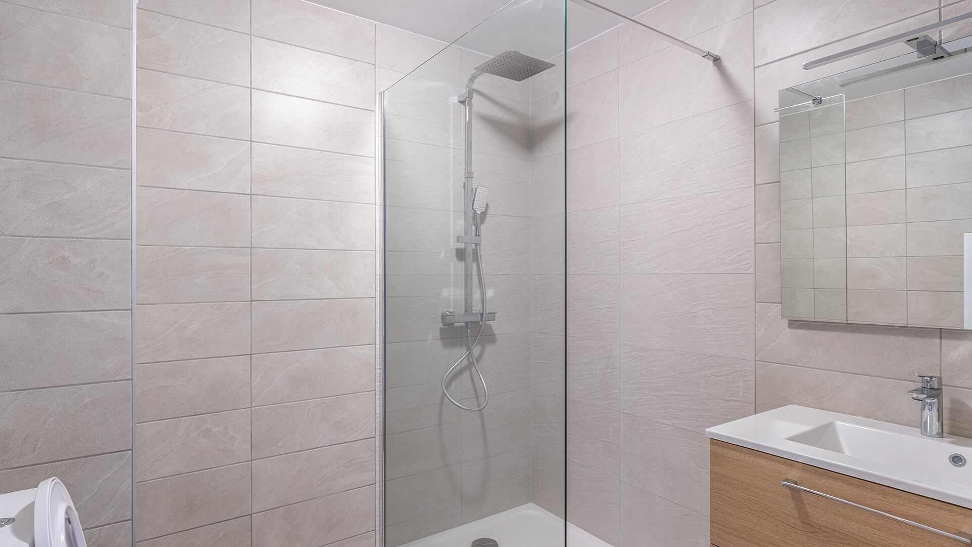 Ein modernes Badezimmer mit einer in Glas eingefassten Dusche, einem Holzkosmetikschrank und einem großen Spiegel.