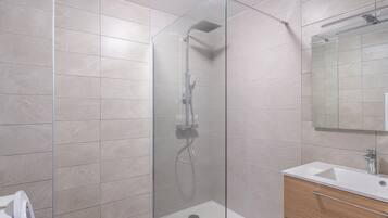 Ein modernes Badezimmer mit einer in Glas eingefassten Dusche, einem Holzkosmetikschrank und einem großen Spiegel.