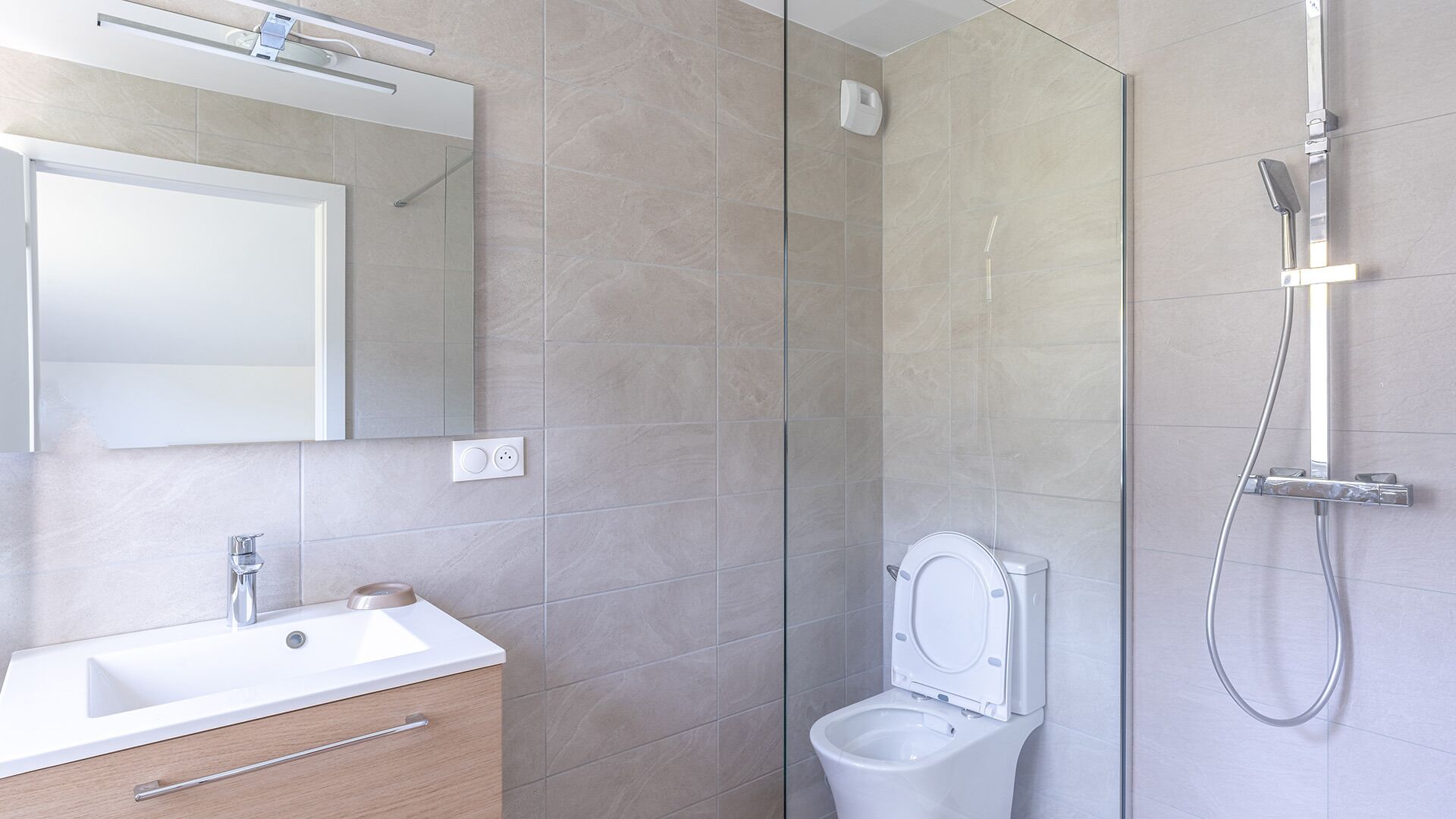 A modern bathroom with a glass shower enclosure, a white toilet, and a vanity with a mirror.