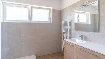A modern bathroom with a white sink, mirror, and towel rack. There are two windows providing natural light.