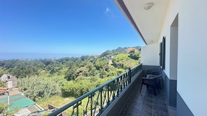 En balkon med udsigt over et frodigt, grønt landskab og fjerne bygninger.