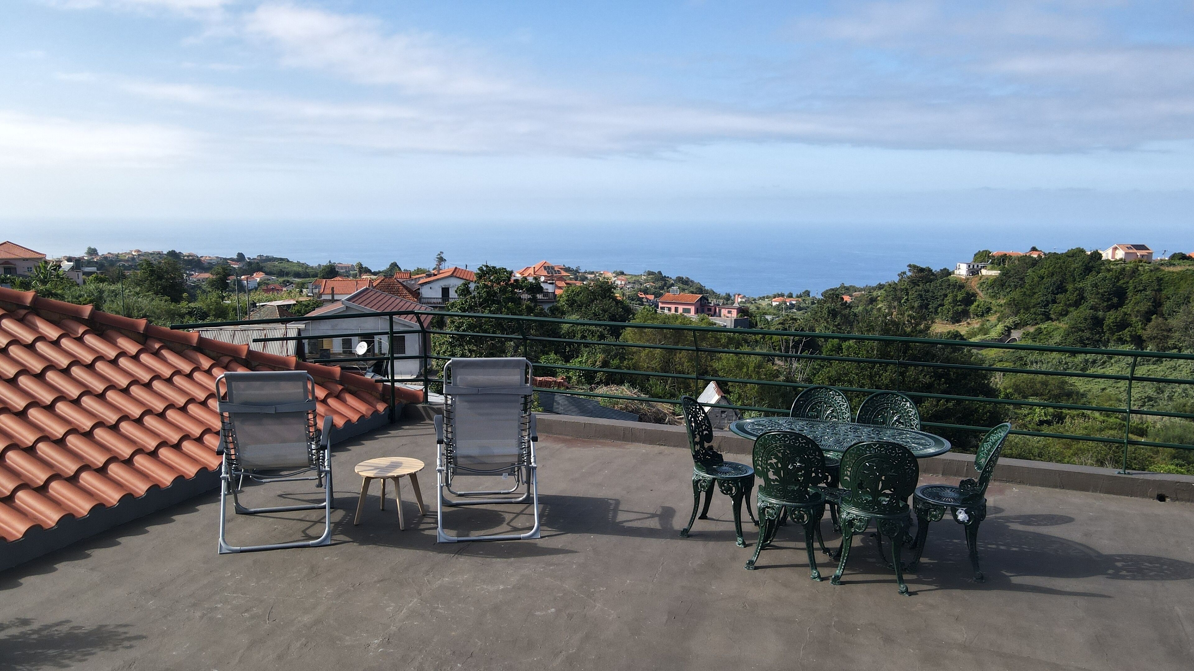 Una terraza en la azotea con mesa y sillas, vista al mar y tejados de tejas rojas.