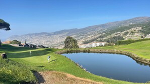 A golf course with a pond, a building with a red roof, and a mountainous backdrop. - Sea and Sun 4 You - Villa Jardim (Santana)