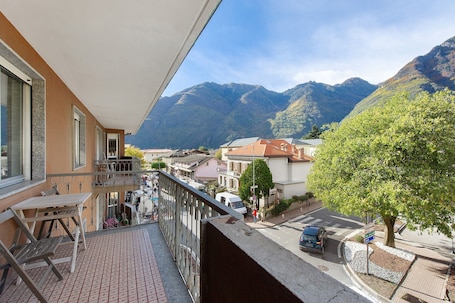 A balcony with a table and chairs, overlooking a street with buildings and mountains in the background.. Three-Room Apartment in Verrès – Modern Comfort with Mountain Views