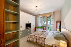 A bedroom with a bed, a TV, a window, and a wooden wardrobe.