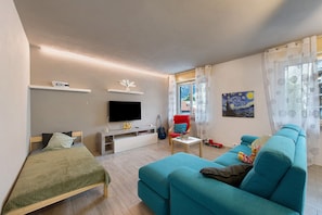 A modern living room with a bed, sofa, TV, and artwork.