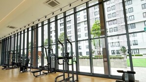 A gym with exercise equipment and large windows offering a view of a building and greenery.
