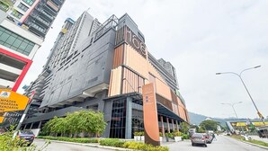 A modern building with a prominent 'Haas' sign, likely a hotel or commercial property, with a parking area in front and a street view with cars and a mountain in the background.