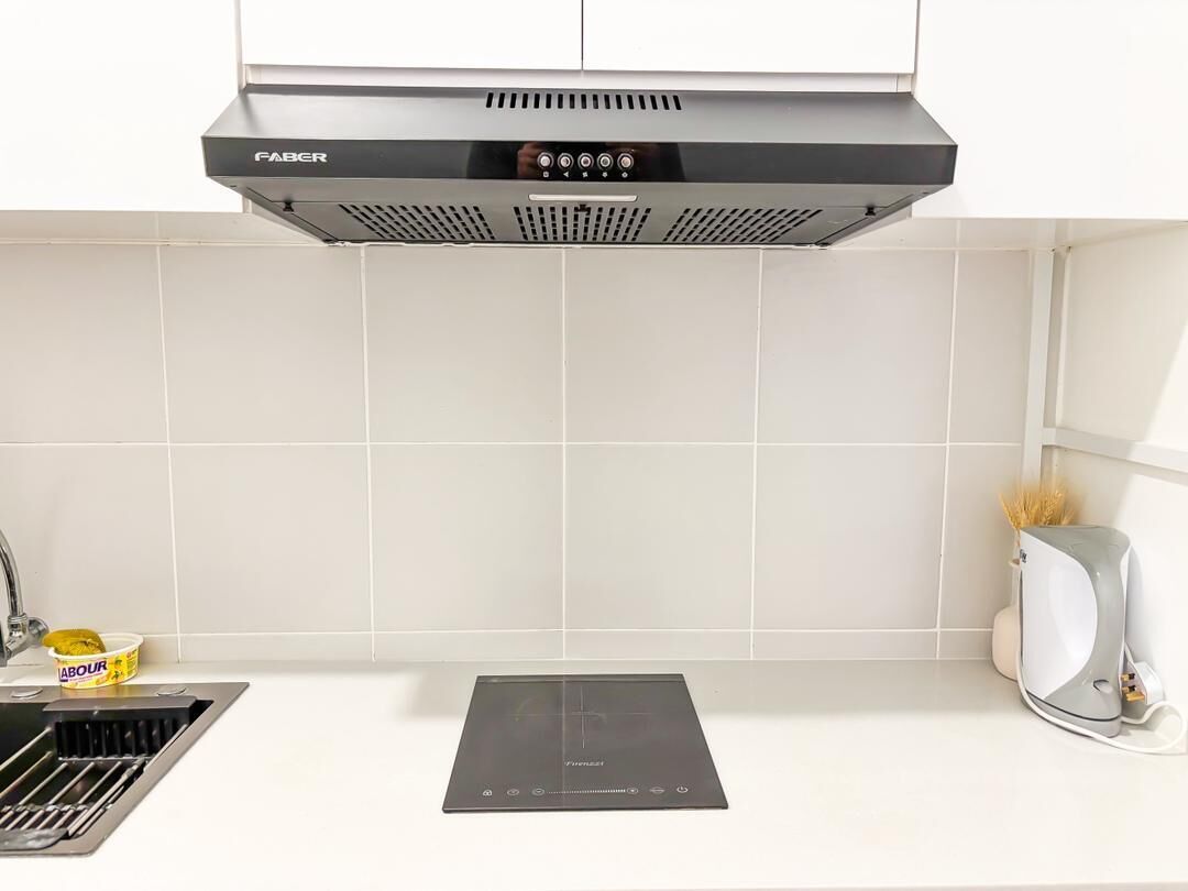 A kitchen with a black range hood, a built-in induction cooktop, and a stainless steel sink.