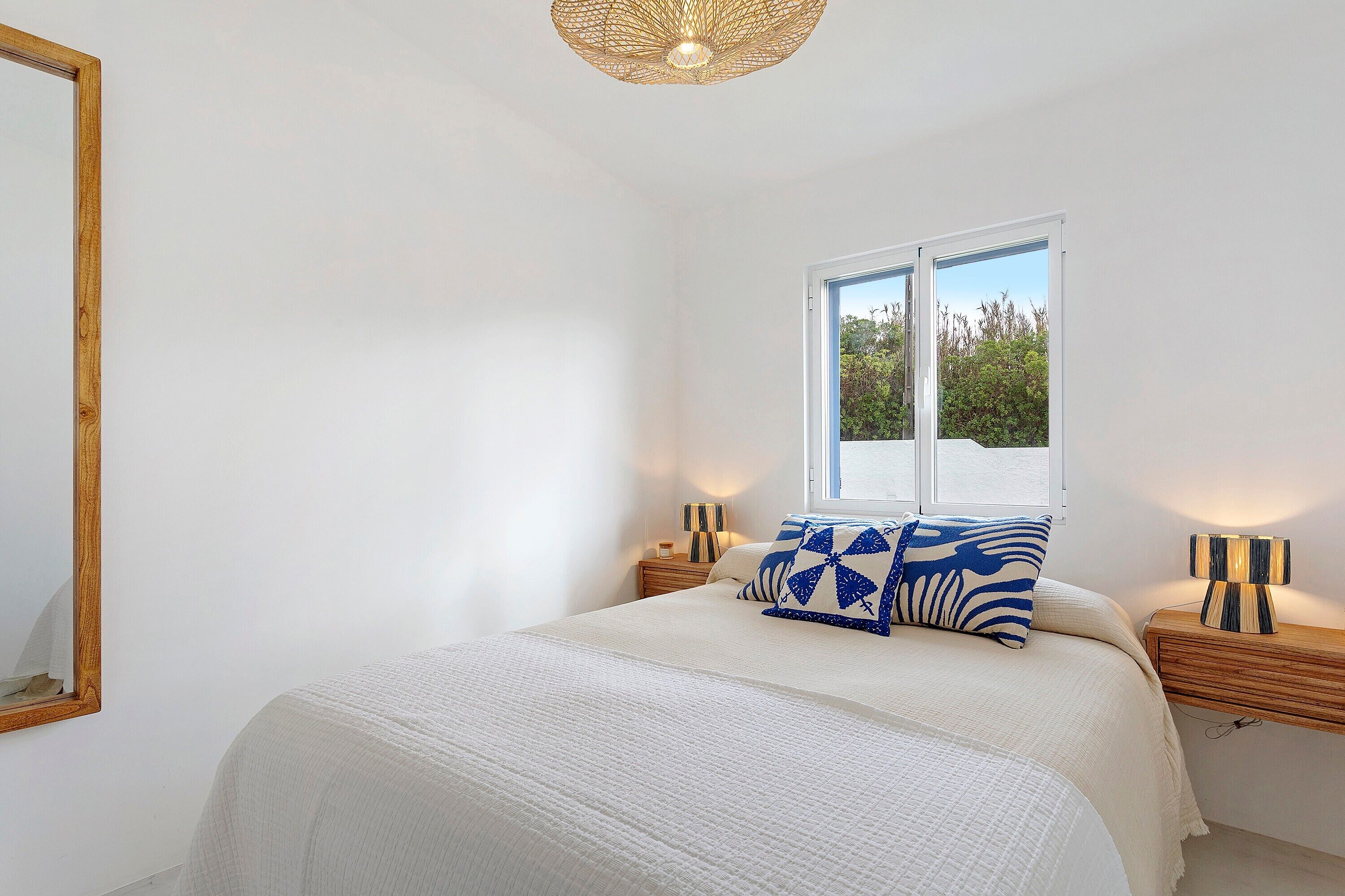 A bedroom with a large bed, a window, a bedside lamp, and a mirror.