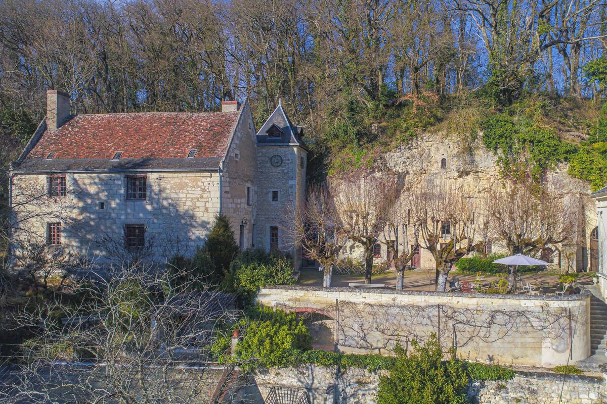A stone building with a red-tiled roof, a stone wall, and a small garden area with a bench and an umbrella.