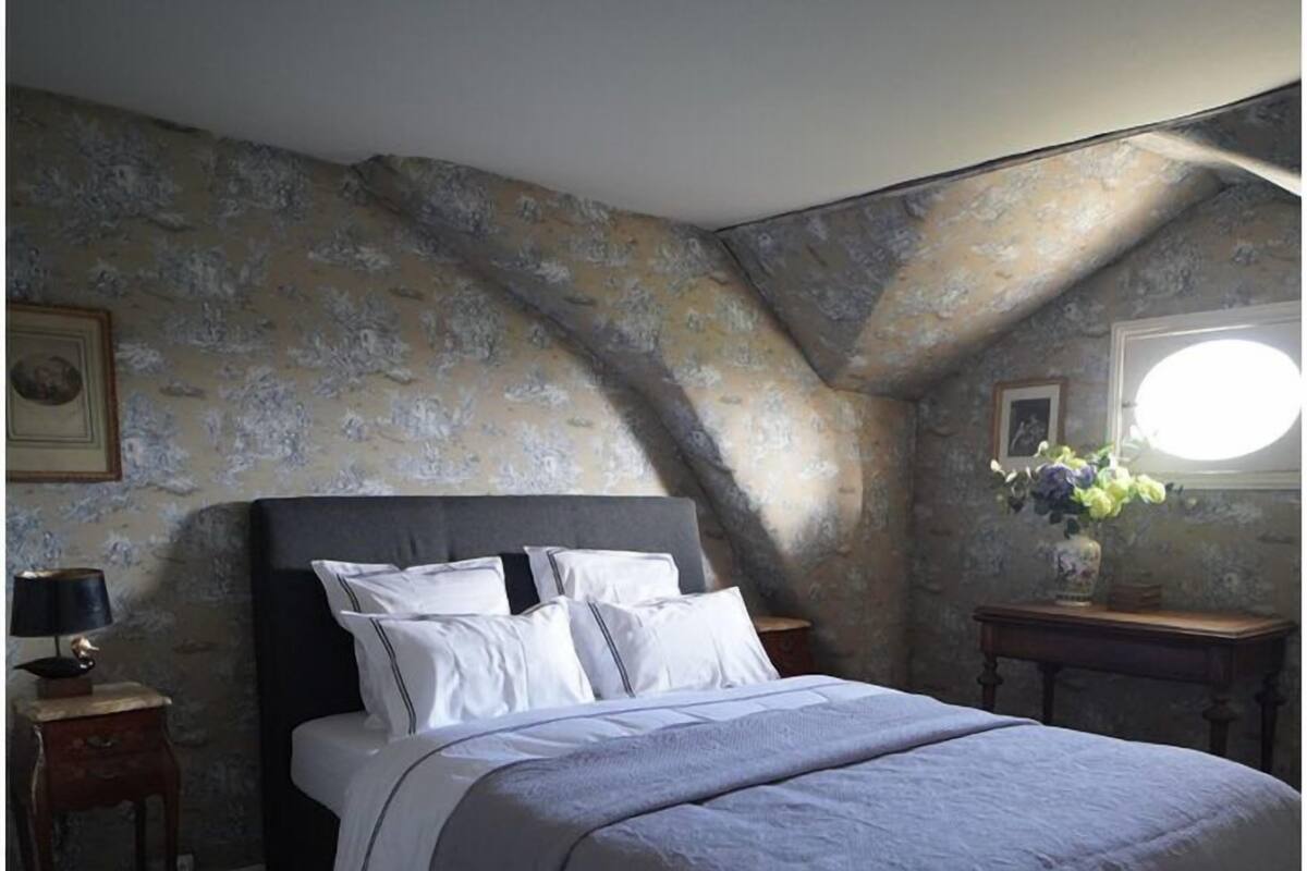 A bedroom with a large bed, a nightstand, a dresser, and a window with a view of the sky.